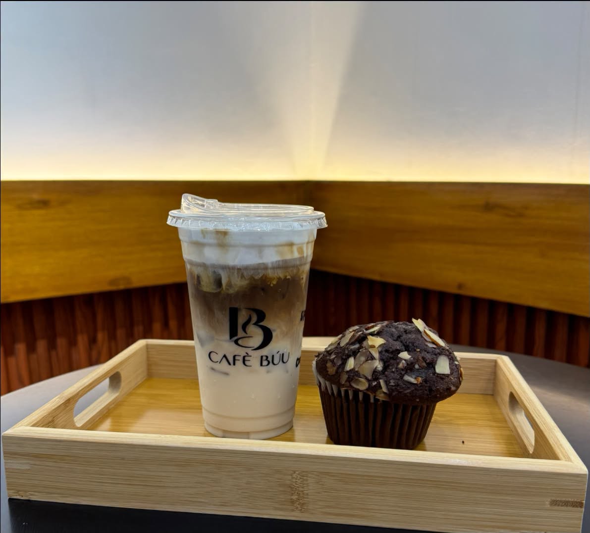 Actual Cafè Búu iced coffee and chocolate muffin on a wooden tray